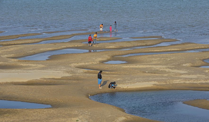 In this Wednesday, Dec. 4, 2019, photo, sightseers plays on a sandbar in the Mekong River in Nakhon Phanom province, northeastern Thailand. Experts say the aquamarine color the Mekong River has recently acquired may beguile tourists but it also indicates a problem caused by upstream dams. The water usually is a yellowish-brown shade due to the sediment it normally carries downstream. But lately it has been running clear, taking on a blue-green hue that is a reflection of the sky. The water levels have also become unusually low, exposing sandbanks in the middle of the river. (AP Photo/Chessadaporn Buasai)
