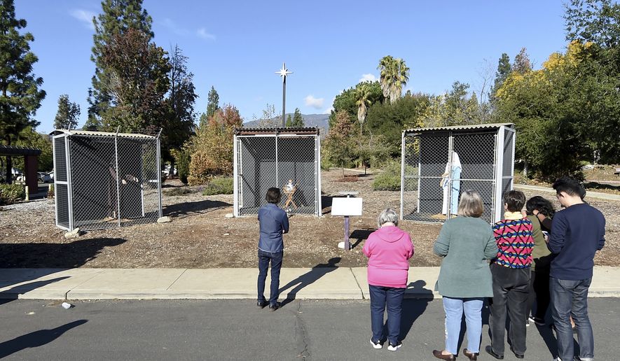 Visitors to a nativity scene displayed outside of Claremont United Methodist Church in Claremont look at baby Jesus, Mary and Joseph as they are displayed in separate cages Monday, Dec. 9, 2019. The church has displayed a controversial nativity scene depicting Mary and Joseph in separate chain link cages with baby Jesus in a separate cage between them.  (Will Lester/The Orange County Register via AP)
