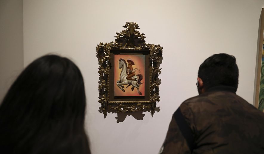 People watch a painting showing 1910-17 Mexican revolutionary hero Emiliano Zapata nude, wearing high heels and a pink, broad-brimmed hat, straddling a horse, in Mexico City, Tuesday, Dec. 10, 2019. The work by Fabian Chairez is part of an exhibit about Zapata in one of Mexico City's premiere arts venues, the Fine Arts Palace. (AP Photo/Eduardo Verdugo)