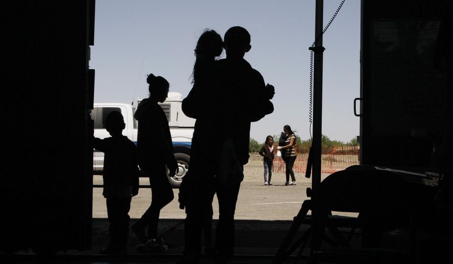 FILE - In this May 22, 2019 file photo migrants mainly from Central America guide their children through the entrance of a World War II-era bomber hanger in Deming, N.M. U.S. lawyers said Wednesday, Dec. 11, 2019, they want a judge to dismiss claims by New Mexico that immigration officials shirked their duties earlier this year by quickly releasing thousands of mostly Central American migrants into communities after they crossed into the United States. (AP Photo/Cedar Attanasio, File)