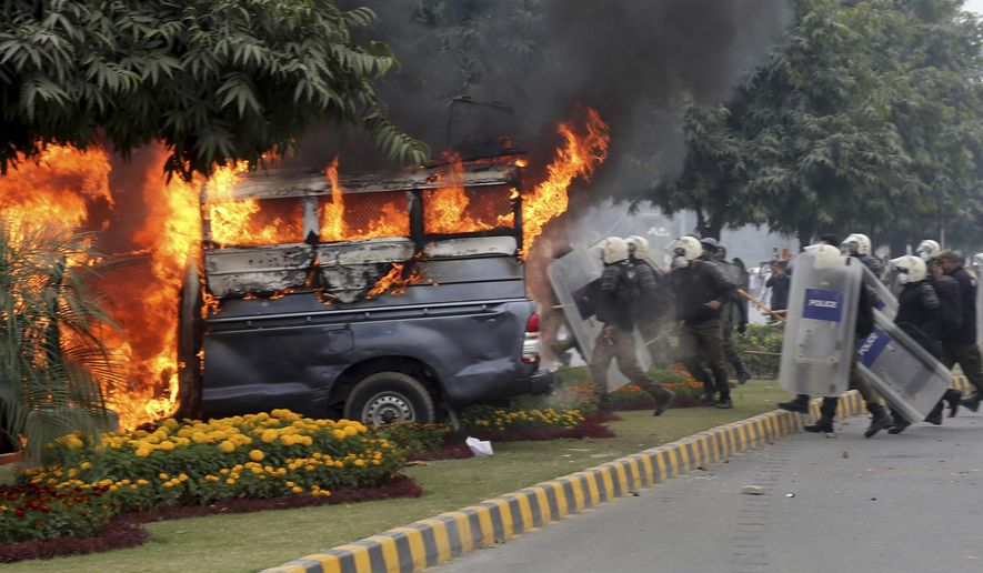 Police officers gather next to a burning police vehicles set on fire by angry lawyers during clashes in Lahore, Pakistan, Wednesday, Dec. 11, 2019. Hundreds of Pakistani lawyers, angered over alleged misbehavior of some doctors toward one of their colleagues last month, stormed a cardiology hospital in the eastern city of Lahore, setting off scuffles with the facility's staff and guards that left heart patients unattended for several hours. (AP Photo/K.M. Chaudary)