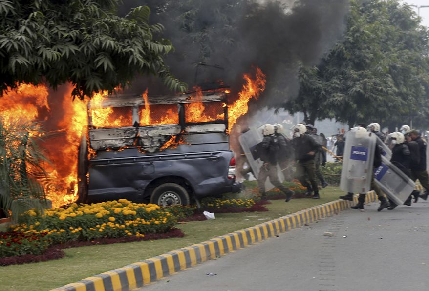 Police officers gather next to a burning police vehicles set on fire by angry lawyers during clashes in Lahore, Pakistan, Wednesday, Dec. 11, 2019. Hundreds of Pakistani lawyers, angered over alleged misbehavior of some doctors toward one of their colleagues last month, stormed a cardiology hospital in the eastern city of Lahore, setting off scuffles with the facility's staff and guards that left heart patients unattended for several hours. (AP Photo/K.M. Chaudary)