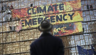 A man looks up as police and fire personnel move in to remove climate activists after they climbed the Europa building during a demonstration outside an EU summit meeting in Brussels, Thursday, Dec. 12, 2019. Greenpeace activists on Thursday scaled the European Union&#39;s new headquarters, unfurling a huge banner warning of a climate emergency hours before the bloc&#39;s leaders gather for a summit focused on plans to combat global warming.(AP Photo/Francisco Seco)
