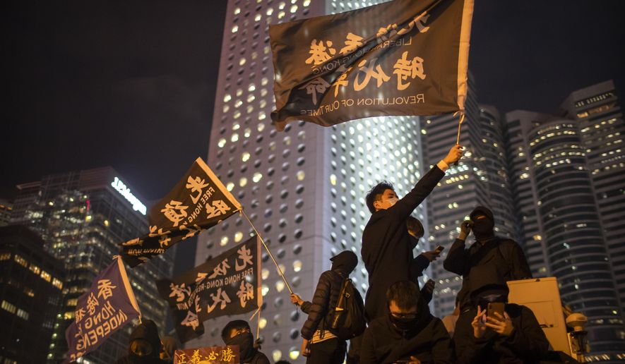 A protestor holds a flag that reads: "Liberate Hong Kong, Revolution of Our Times" at a rally in Hong Kong, Thursday, Dec. 12, 2019. Protesters in Hong Kong have written hundreds of Christmas cards for detainees jailed in the city's pro-democracy movement. At a rally on Thursday night, protesters promised on the cards that detainees won't be forgotten as they face spending the festive season behind bars. (AP Photo/Mark Schiefelbein)