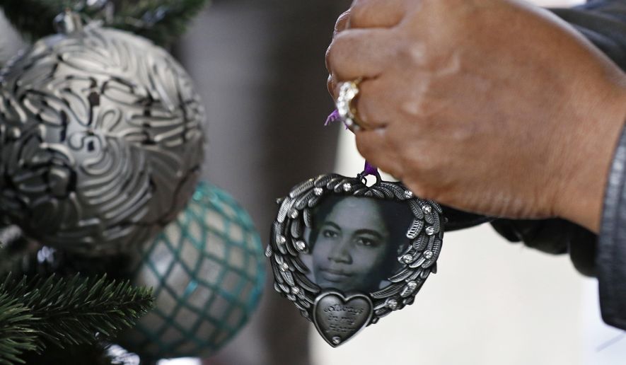 A family member hangs the photograph ornament of a loved one, during a tree lighting ceremony honoring victims of violent criminal acts and recognizing the surviving family members of the homicide victims, Thursday, Dec. 12, 2019, in Jackson, Miss. (AP Photo/Rogelio V. Solis)