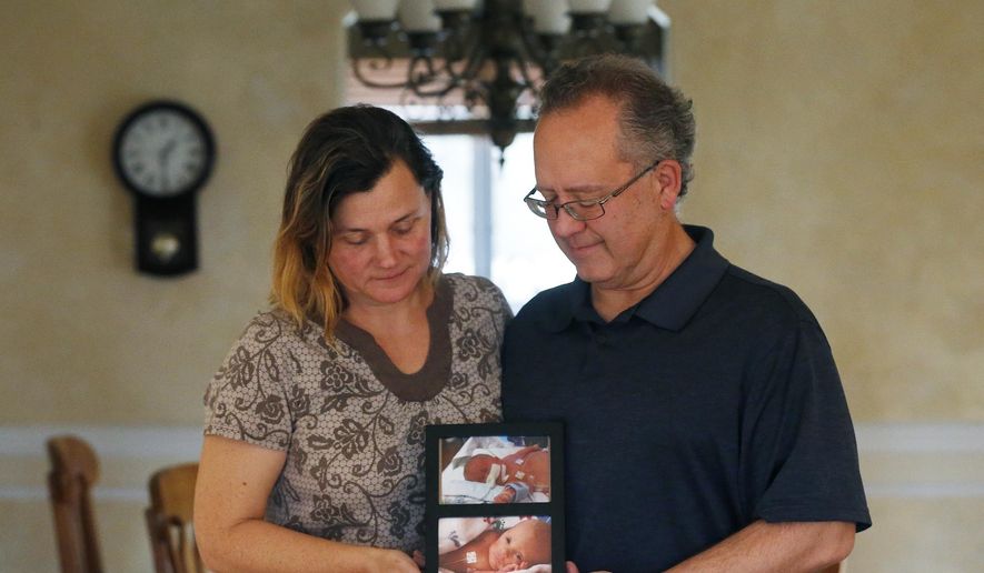 Jim and Sue LaDeur, pose with photos of their twin babies, Billy, top, and Matt, Thursday, Dec. 12, 2019, at their home in Elmhurst, Ill. Billy and Matt were born on November 18, 2014. The suburban Chicago couple, whose house was ransacked this week, is begging whoever made off with some belongings inside to return just one thing: The small white box containing the ashes of their infant son Billy. (Stacey Wescott/Chicago Tribune via AP)