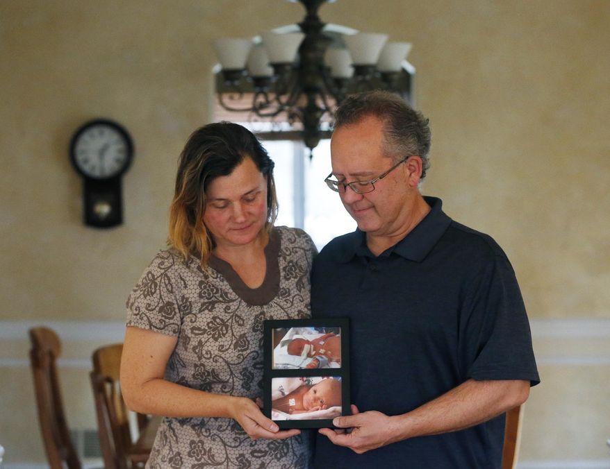 Jim and Sue LaDeur, pose with photos of their twin babies, Billy, top, and Matt, Thursday, Dec. 12, 2019, at their home in Elmhurst, Ill. Billy and Matt were born on November 18, 2014. The suburban Chicago couple, whose house was ransacked this week, is begging whoever made off with some belongings inside to return just one thing: The small white box containing the ashes of their infant son Billy. (Stacey Wescott/Chicago Tribune via AP)