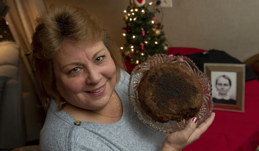 In this Dec. 9, 2019, photo Julie Ruttinger, of Tecumseh, Mich., holds a 141-year-old fruitcake, a family heirloom baked by her great-great-grandmother, Fidelia Ford, in 1878. Fidelia, pictured at left, died before the cake was served and the family, out of respect of her memory, decided not to eat it and has instead passed it down for generations. It resides in a glass case with the date of its creation affixed to the top. (David Guralnick/Detroit News via AP)