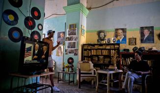 FILE - In this Jan. 20, 2017 file photo, a man watches President Donald J. Trump&#39;s inauguration speech on television, as he sits under photographs of Cuba&#39;s President Raul Castro, top right, Fidel Castro, top center, and Camilo Cienfuegos, in Havana, Cuba. Trump has spent roughly as much time undoing detente as former President Barack Obama spent constructing it, and relations between the two countries are at one of their lowest points since the end of the Cold War.  (AP Photo/Ramon Espinosa, File)