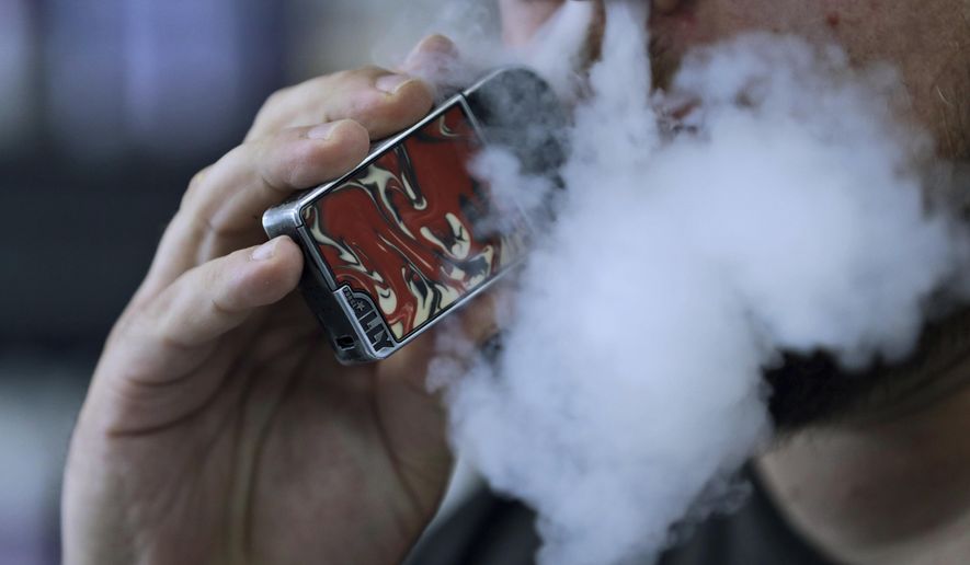 In this Friday, Oct. 4, 2019 file photo, a man using an electronic cigarette exhales in Mayfield Heights, Ohio. A judge has cleared the way for Montana to temporarily ban the sale of flavored e-cigarettes and other flavored vaping products. State officials say they plan to implement the ban Wednesday, Dec. 18, 2019. (AP Photo/Tony Dejak,File)