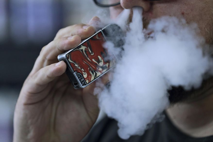 In this Friday, Oct. 4, 2019 file photo, a man using an electronic cigarette exhales in Mayfield Heights, Ohio. A judge has cleared the way for Montana to temporarily ban the sale of flavored e-cigarettes and other flavored vaping products. State officials say they plan to implement the ban Wednesday, Dec. 18, 2019. (AP Photo/Tony Dejak,File)
