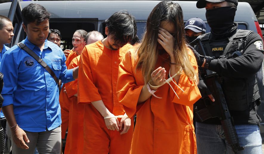 Indonesian custom officers escort foreign suspects for drug smuggling charges in Bali, Indonesia, Wednesday, Dec. 18, 2019. Indonesian authorities say they have arrested six foreigners for allegedly trying to smuggle drugs onto the tourist island of Bali. The foreigners, a Swiss man, a Thai man, a Singaporean woman, a Chilean man and two Hong Kong men, wearing orange detainees uniform were paraded with their feet and hands tied, at a news conference.(AP Photo/Firdia Lisnawati)