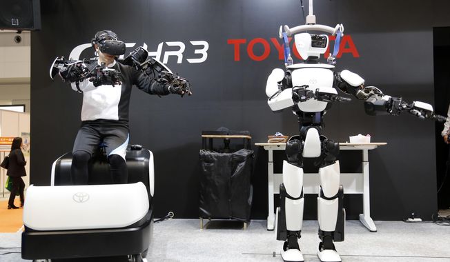 In this Dec. 18, 2019, photo, Toyota Motor Corp.&#x27;s human-shaped T-HR3 robot, right, is remotely controlled by its staff member, left, during a demonstration in Tokyo. Toyota&#x27;s upgraded version of the human-shaped T-HR3 now has faster and smoother finger movements because the wearable remote-control device has become lighter and easier to use. The person wearing a headset and wiring made the robot move in exactly the same way he was moving, waving or making dance-like movements, as sensors sent computerized signals to the robot of what they detected as human movements. (AP Photo/Yuri Kageyama)