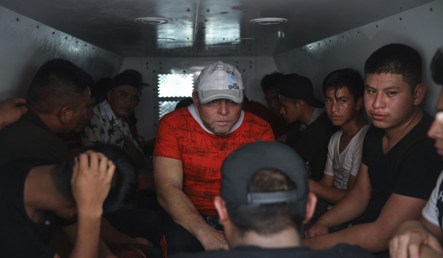 In this Nov. 26, 2019, file photo, migrants are held in a van of the National Migration Institute after they were found in the cargo hold of a truck where dozens of Central American migrants were being smuggled, at an immigration checkpoint in Medellin de Bravo, Veracruz state, Mexico. Except for official border crossings, nearly every mile of river, desert and mountain along the U.S.-Mexican border is under the control of Mexico's organized crime rings, which decide who can cross and how much they will pay. (AP Photo/Felix Marquez) ** FILE **