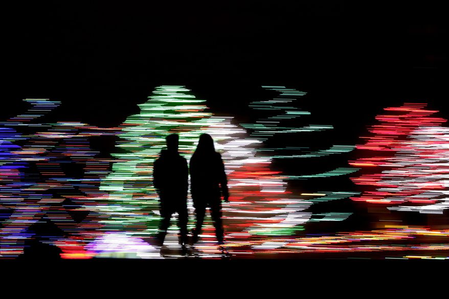 FILE -In this Dec. 12, 2019 file photo taken with a long exposure, people are silhouetted against a Christmas display, at a park in Lenexa, Kan. Most Americans say the holiday season makes them feel very grateful and generous — but many report feeling stressed, too according to a new poll from The Associated Press-NORC Center for Public Affairs Research. (AP Photo/Charlie Riedel, File)