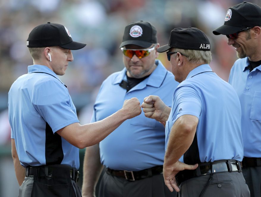 FILE - In this July 10, 2019, file photo, home plate umpire Brian deBrauwere, left, huddles with officials while wearing an earpiece connected to a ball and strikes calling system before the Atlantic League All-Star minor league baseball game in York, Pa. DeBrauwere wore the earpiece connected to an iPhone in his ball bag which relayed ball and strike calls upon receiving it from a TrackMan computer system that uses Doppler radar. The independent Atlantic League became the first American professional baseball league to let the computer call balls and strikes during the all star game. Umpires agreed to cooperate with Major League Baseball in the development and testing of an automated ball-strike system as part of a five-year labor contract announced Saturday, Dec. 21, two people familiar with the deal told The Associated Press. The Major League Baseball Umpires Association also agreed to cooperate and assist if Commissioner Rob Manfred decides to utilize the system at the major league level. The people spoke on condition of anonymity because those details of the deal, which is subject to ratification by both sides, had not been announced. (AP Photo/Julio Cortez)