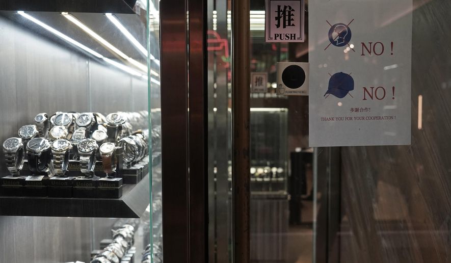 In this Wednesday, Dec. 18, 2019, photo, a notice is attached to the front door demanding no hats and masks allowed in the watch store to help prevent robberies after the shop was attacked by armed robbers recently in Mongkok, a shopping district of Hong Kong. Sellers of luxury goods that are easily peddled by thieves have become targets for armed robbery gangs during the pro-democracy protests that have been gripping Hong Kong. (AP Photo/Kin Cheung)