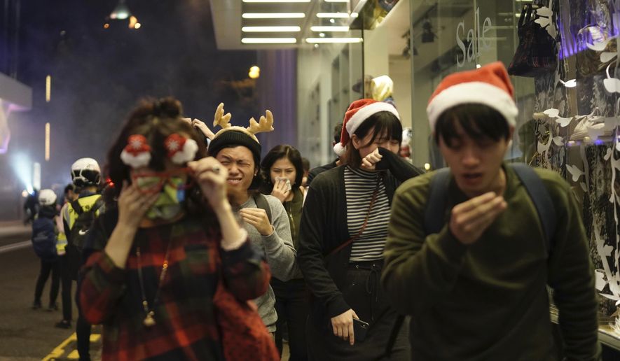 Residents dressed for Christmas festivities react to tear gas as police confront protesters on Christmas Eve in Hong Kong on Tuesday, Dec. 24, 2019. More than six months of protests have beset the city with frequent confrontations between protesters and police. (AP Photo/Kin Cheung)
