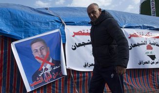 A protester walks past a poster with a defaced picture of the governor of the southern Basra province Asaad al-Eidani and Arabic that reads &amp;quot;rejected by the people,&amp;quot; during the ongoing protests, in Tahrir square, in Baghdad, Iraq, Wednesday, Dec. 25, 2019. An Iranian-backed bloc in Iraq’s parliament proposed al-Eidani as the country’s next prime minister. However, the nomination was promptly rejected by Iraqi protesters who want an independent candidate to take over the government. Earlier on Wednesday, outgoing higher education minister, who had also been rejected by protesters on the streets, withdrew his nomination for prime minister. (AP Photo/Nasser Nasser)