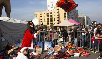 In this Sunday, Dec. 22, 2019, photo, volunteer Ibtisam Nablussi tosses a Christmas present, as anti-government protesters distribute clothing to the needy ahead of Christmas, at Martyrs Square in Beirut, Lebanon. Lebanon is entering its third month of protests, the economic pinch is hurting everyone, and the government is paralyzed. So people are resorting to what they&#39;ve done in previous crises: They rely on each other, not the state. (AP Photo/Maya Alleruzzo)
