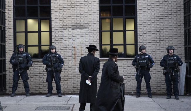 FILE - In this Dec. 11, 2019 file photo, Orthodox Jewish men pass New York City police guarding a Brooklyn synagogue prior to a funeral for Mosche Deutsch in New York. Deutsch, a rabbinical student from Brooklyn, was killed in the shooting inside a Jersey City, N.J. market. New York City is increasing its police presence in some Brooklyn neighborhoods with large Jewish populations after a number of possibly anti-Semitic attacks during the Hanukkah holiday. (AP Photo/Mark Lennihan, File)