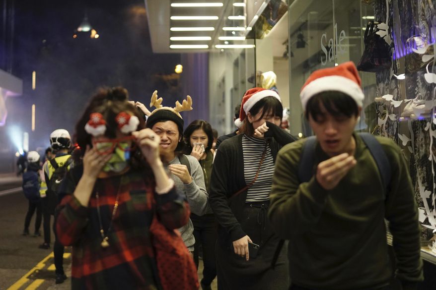 Residents dressed for Christmas festivities react to tear gas as police confront protesters on Christmas Eve in Hong Kong on Tuesday, Dec. 24, 2019. More than six months of protests have beset the city with frequent confrontations between protesters and police. (AP Photo/Kin Cheung)