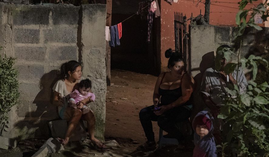A family sits outside their home as forensic workers investigate a body at a crime scene in the Rivera Hernandez neighborhood of San Pedro Sula, Honduras on Nov. 30, 2019. MS-13. Mara 18. Los Vatos Locos _ The Crazy Guys. The gangs' shifting lines of control dodge and weave through Rivera Hernandez, a place where even the police are afraid. (AP Photo/Moises Castillo)