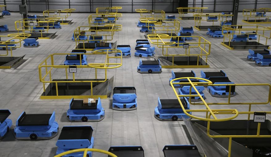 In this Dec. 17, 2019, photo dozens of Amazon robots transport packages from workers to chutes that are organized by zip code, at an Amazon warehouse facility in Goodyear, Ariz. Amazon and its rivals are increasingly requiring warehouse employees to get used to working with robots. The company now has more than 200,000 robotic vehicles it calls “drives” that are moving goods through its delivery-fulfillment centers around the U.S. (AP Photo/Ross D. Franklin)