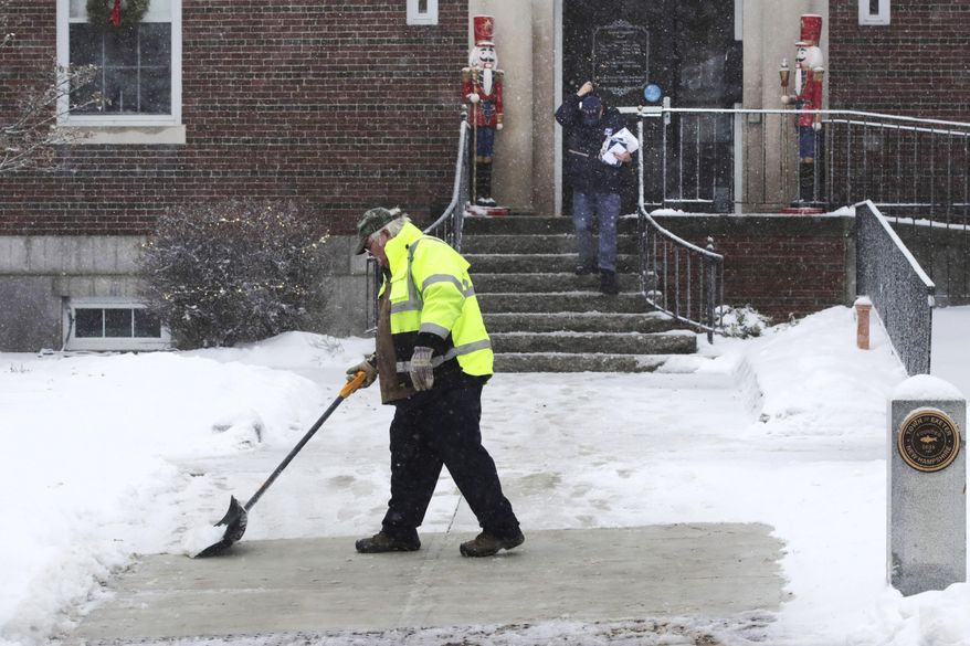 A worker shovels a coating of crusty snow from the walkway outside town hall during a snow storm in Exeter, N.H., Monday, Dec. 30, 2019. The southern New Hampshire area received a coating of snow and ice during the winter storm. (AP Photo/Charles Krupa)