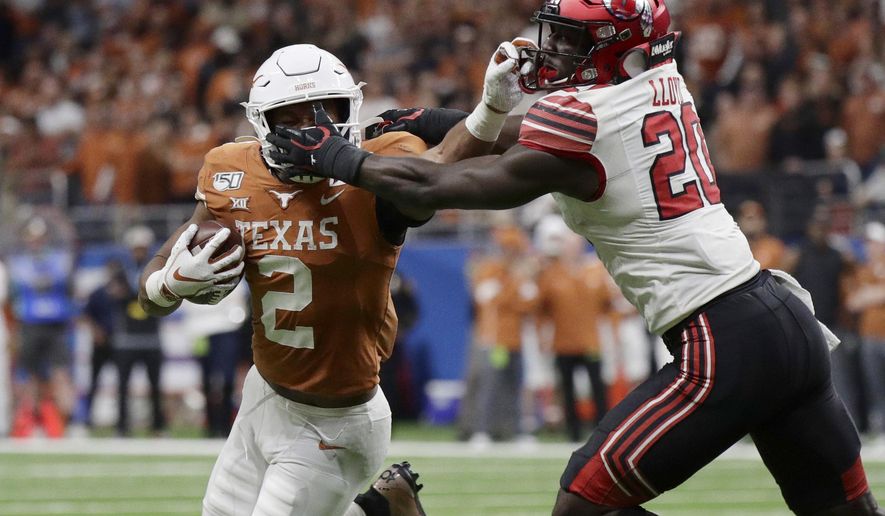 Texas running back Roschon Johnson (2) has his face mask grabbed by Utah linebacker Devin Lloyd (20) during the second half of the Alamo Bowl NCAA college football game in San Antonio, Tuesday, Dec. 31, 2019. (AP Photo/Eric Gay)
