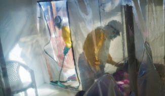 In this July 13, 2019, file photo, health workers wearing protective suits tend to an Ebola victim kept in an isolation cube in Beni, Congo. (AP Photo/Jerome Delay, File)