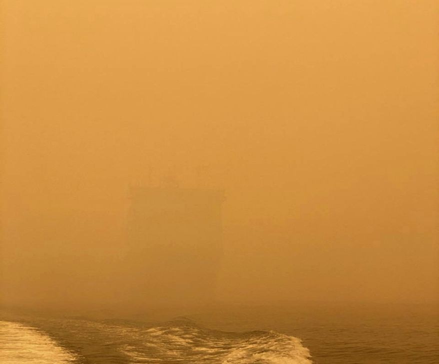 In this photo provided by the Australian Defence Force, HMAS Choules appears as a ghostly figure through smoke haze off the coast of Mallacoota, Australia, Thursday, Jan. 2, 2020. The Australian Defence Force is moving naval assets to Mallacoota on a supply mission that would last two weeks and helicopters would also fly in more firefighters since roads were inaccessible due to wildfires. (Australian Defence Force via AP)