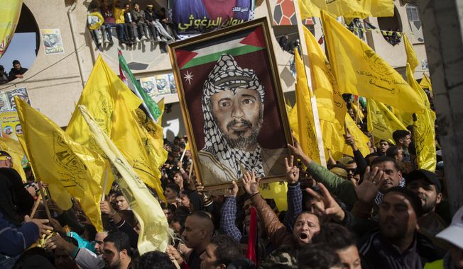 A Palestinian carries a picture of the late Palestinian leader Yasser Arafat, during a rally marking the 55th anniversary of the Fatah movement founding, in Gaza City, Wednesday, Jan. 1, 2020. Fatah is a secular Palestinian party and former guerrilla movement founded by Arafat, in Gaza City, Wednesday, Jan. 1, 2020. (AP Photo/Khalil Hamra)