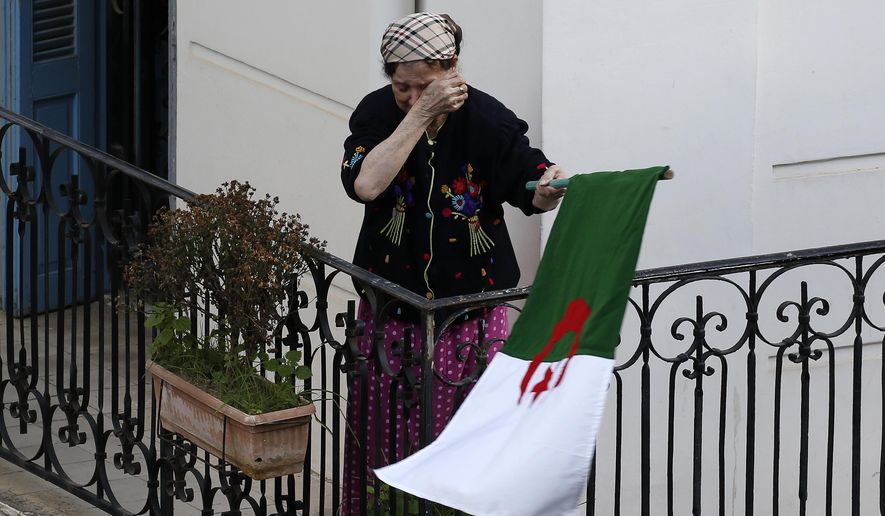 A woman wipes her face while carrying a national flag as protesters take to the streets in the capital Algiers to reject the presidential elections and protest against the government, in Algeria, Friday, Dec. 27, 2019. (AP Photo/Toufik Doudou)
