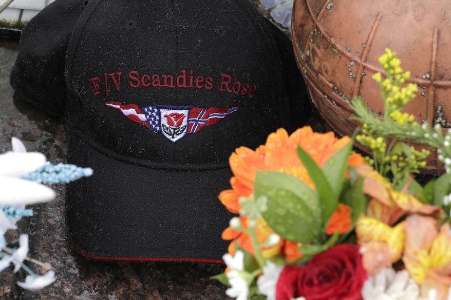 Rain drops gather on a ball cap with the name of the crab fishing boat Scandies Rose, a 130-foot crab fishing boat from Dutch Harbor, Alaska, that sank on New Year's Eve, as the hat rests near some flowers and a fishing float at the Seattle Fishermen's Memorial, Thursday, Jan. 2, 2020, in Seattle. (AP Photo/Ted S. Warren)