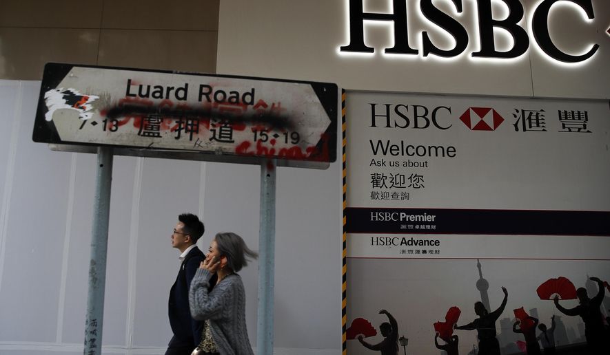 People walk by a vandalized road sign near a HSBC Bank branch covered by panels after damaged by pro-democracy protesters in Hong Kong, Saturday, Jan. 4, 2020. The months-long pro-democracy movement has extended into 2020 with further mass demonstrations. (AP Photo/Andy Wong)