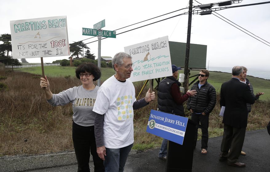 FILE - In this Feb. 10, 2014, file photo, Julie Graves, left, of Albany, Calif., and Chris Adams, second from left, of Berkeley, Calif., hold up signs in support of a beach access bill near Martin's Beach in Half Moon Bay, Calif. California officials are suing a billionaire who has been fighting for more than a decade to keep a secluded beach to himself, a move designed to ensure that the public always has access the scenic stretch of sand. The lawsuit was filed Monday, Jan. 6, 2020, on behalf of the California State Lands Commission and Coastal Commission. (AP Photo/Eric Risberg, File)