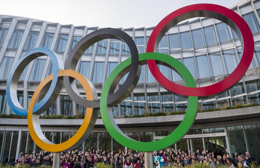Young people pose behind the Olympic Rings during the Torch Tour ahead of the 2020 Winter Youth Olympic Games, front of the Olympic House, in Lausanne, Switzerland, Wednesday, Jan. 8, 2020. The 2020 Winter Youth Olympic Games take place in Lausanne from Jan. 9 to Jan. 22, 2020. (Jean-Christophe Bott/Keystone via AP)