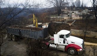 FILE - In this Feb. 8, 2019, file photo, an excavator loads debris onto a truck while clearing a property burned by the Camp Fire in Paradise, Calif. A $13.5 billion settlement covering most of the losses from a series of catastrophic wildfires that drove Pacific Gas and Electric into bankruptcy is turning into a financial tug of war pitting the interests of U.S. taxpayers against the disaster victims still trying to rebuild their lives. (AP Photo/Noah Berger, File)