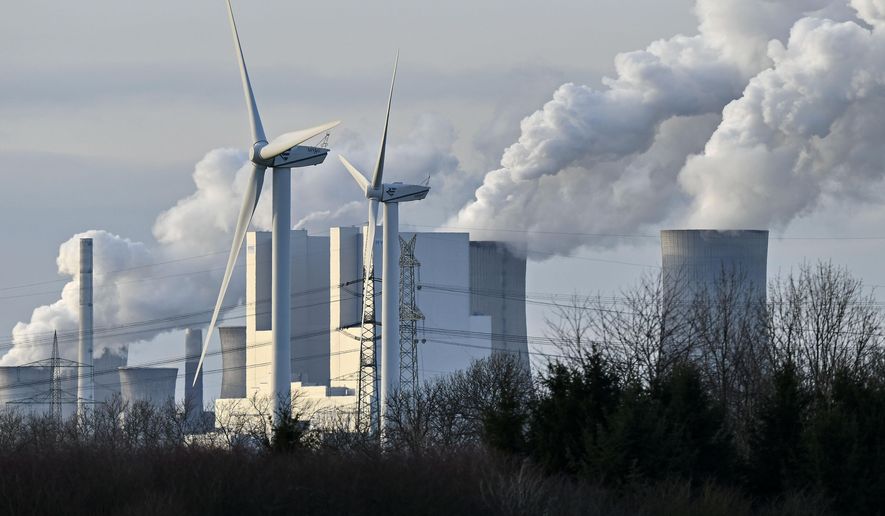 The RWE Niederaussem lignite-fired power station releases steam, behind two renewable energy producing wind turbines in Bergheim, Germany, Monday, Jan. 13, 2020. Germany plans an entirely coal phase out and to shut down all remaining coal-fired plants by 2038. (AP Photo/Martin Meissner)