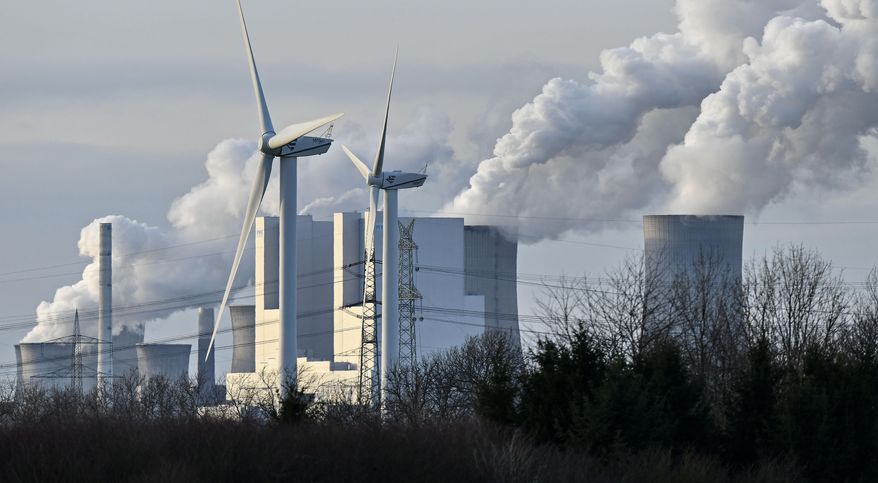 The RWE Niederaussem lignite-fired power station releases steam, behind two renewable energy producing wind turbines in Bergheim, Germany, Monday, Jan. 13, 2020. Germany plans an entirely coal phase out and to shut down all remaining coal-fired plants by 2038. (AP Photo/Martin Meissner)