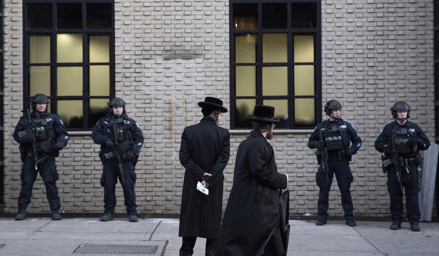 FILE - In this Dec. 11, 2019 file photo, Orthodox Jewish men pass New York City police guarding a Brooklyn synagogue prior to a funeral for Mosche Deutsch, a rabbinical student from Brooklyn who was killed in a shooting at a Jersey City, N.J. market. On Wednesday, Jan. 15, 2019, a group of security experts recommended that Jewish congregations opting to deploy armed security personnel in the wake of deadly attacks on synagogues should — if possible -- use uniformed law enforcement officers rather than private guards or volunteers from the community. (AP Photo/Mark Lennihan, File)