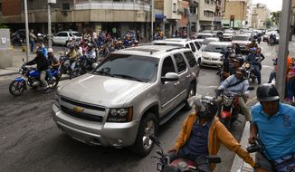Journalists on motorbikes follow a caravan of opposition lawmakers on their way to the National Assembly in Caracas, Venezuela, Wednesday, Jan. 15, 2020. The caravan returned to an opposition headquarter after government supporters hurl stones at the vehicles. (AP Photo/Matias Delacroix)
