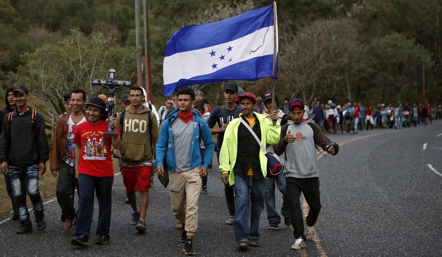 Honduran migrants walk north along a road in hopes of reaching the distant United States, one carrying a Honduran flag, as they leave Esquipulas, Guatemala, just after sunrise Friday, Jan. 17, 2020. The group departed San Pedro Sula on Jan. 15. (AP Photo/Moises Castillo)