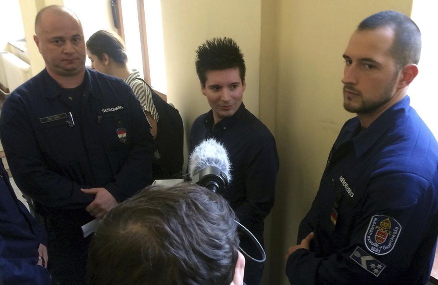 FILE - In this Tuesday, March 5, 2019 file photo, Portuguese Rui Pinto, center, is surrounded by police officers in the hallway of the Metropolitan Court in Budapest, Hungary, as he awaits a decision on his extradition to Portugal. Pinto denies wrongdoing. A Portuguese judge ruled Friday Jan. 17, 2020, that prosecutors have enough evidence incriminating Rui Pinto, an alleged hacker charged with publishing internal documents, to stand trial. (AP Photo/Pablo Gorondi, File)