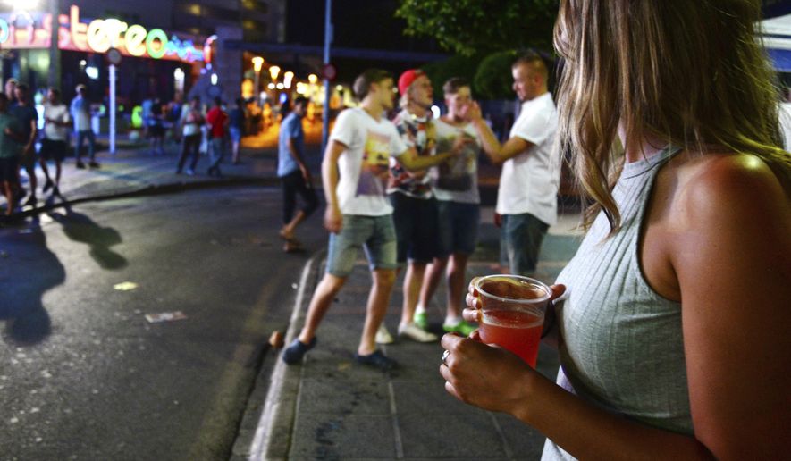 FILE - In this June 10, 2015 file photo, tourists stand on the street in Magaluf, Calvia on the Spanish Balearic island of Mallorca, Spain. Authorities in Spain´s tourist-magnet Balearic Islands are clamping down on binge-drinking tourism in three hot-spots. The regional government has passed a law prohibiting the organization and promotion of pub crawls and publicity promoting the consumption of alcohol by means of ‘open bars’ and ‘happy hours&#x27;. (AP Photo/Joan Llado, File)