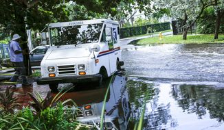 FILE - In this June 19, 2019 file photo, a postal worker returns to their truck parked on a flooded street in Miami caused by high tides. Flooding due to climate change-related sea level rising, the erosion of natural barriers and long-periods of rain pose substantial economic risks to Florida, particularly its real estate value, according to two new reports released last week. (AP Photo/Ellis Rua, File)