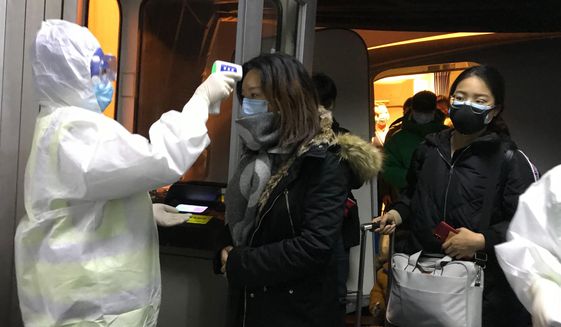 Health Officials in hazmat suits check body temperatures of passengers arriving from the city of Wuhan Wednesday, Jan. 22, 2020, at the airport in Beijing, China. Nearly two decades after the disastrously-handled SARS epidemic, China’s more-open response to a new virus signals its growing confidence and a greater awareness of the pitfalls of censorship, even while the government is as authoritarian as ever. (AP Photo Emily Wang)