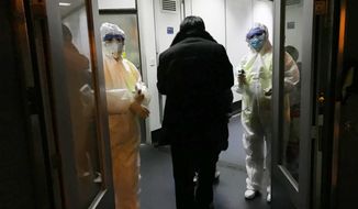 Health Officials in hazmat suits wait at the gate to check body temperatures of passengers arriving from the city of Wuhan Wednesday, Jan. 22, 2020, at the airport in Beijing, China. Nearly two decades after the disastrously-handled SARS epidemic, China’s more-open response to a new virus signals its growing confidence and a greater awareness of the pitfalls of censorship, even while the government is as authoritarian as ever. (AP Photo Emily Wang)