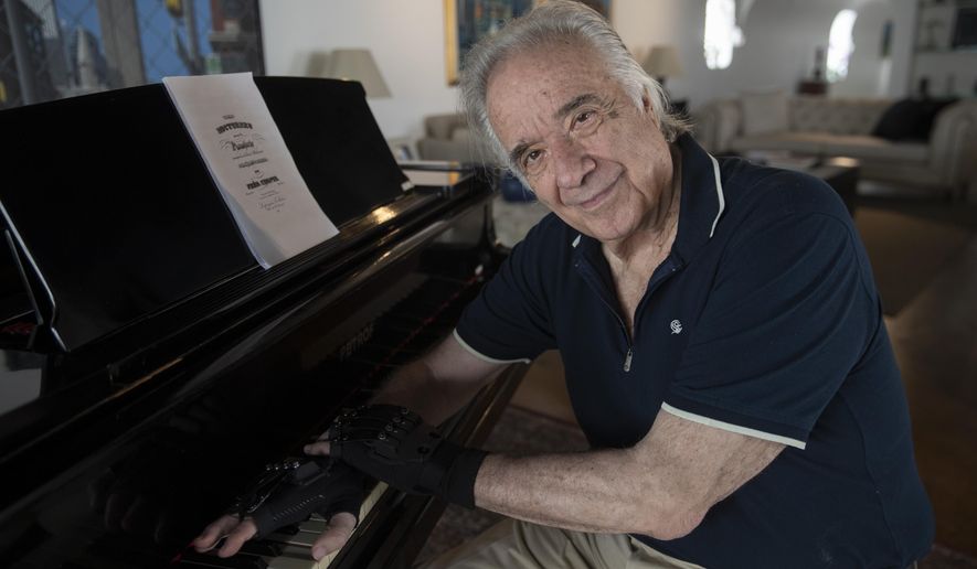 Brazilian pianist Joao Carlos Martins poses for pictures wearing bionic gloves, at his home in Sao Paulo, Brazil, Wednesday, Jan. 22, 2020. Martins, 79, was for decades Brazil&#39;s most acclaimed pianist, but an accident an a degenerative disease forced him to stop playing with both hands since 1998. That changed a few months ago when a new friend came to him with a pair bionic gloves that suit him perfectly. He can now play again with nine out of ten fingers. (AP Photo/Andre Penner)